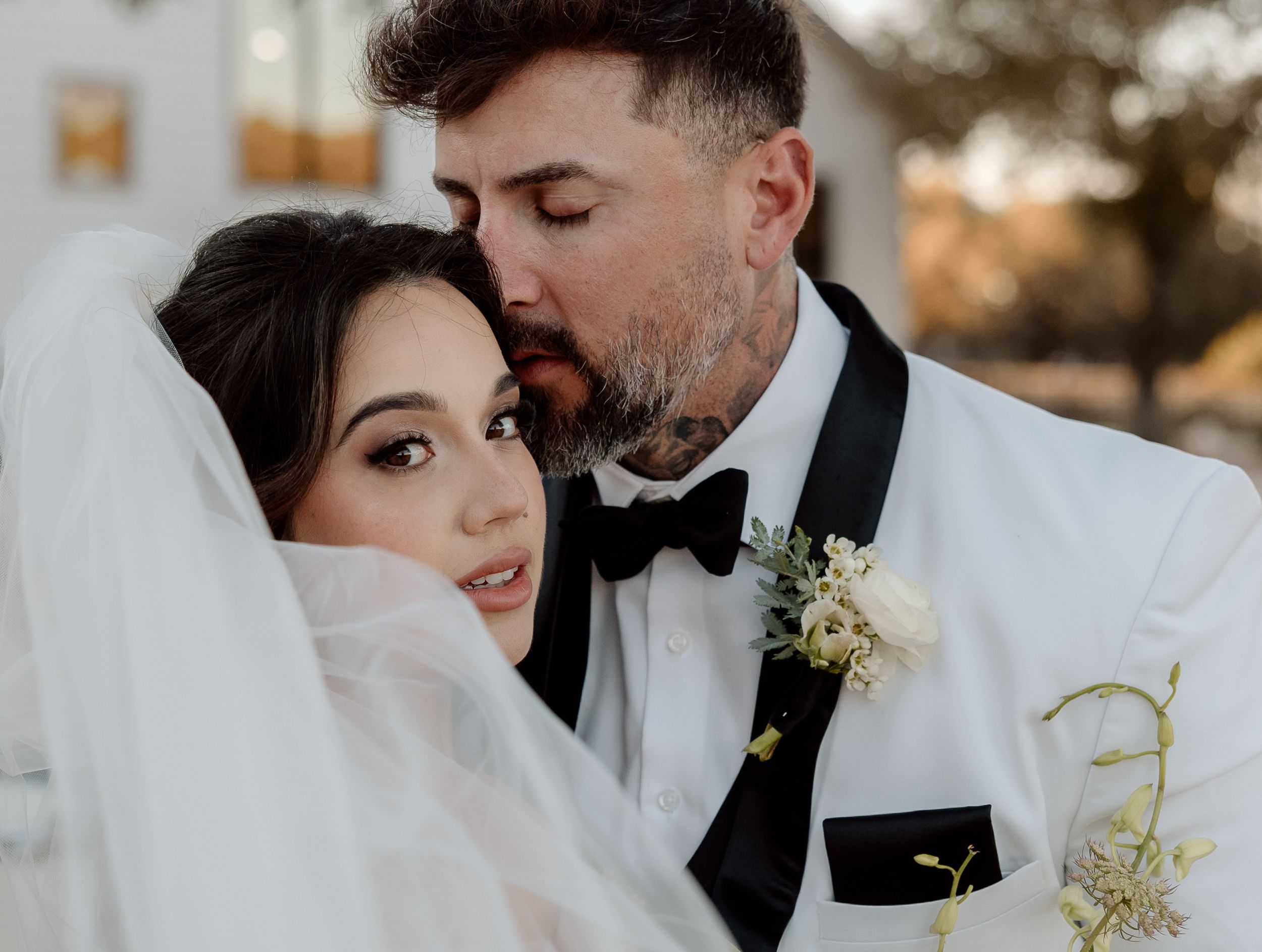 A romantic wedding portrait showing a tender moment between newlyweds in white attire at sunset.