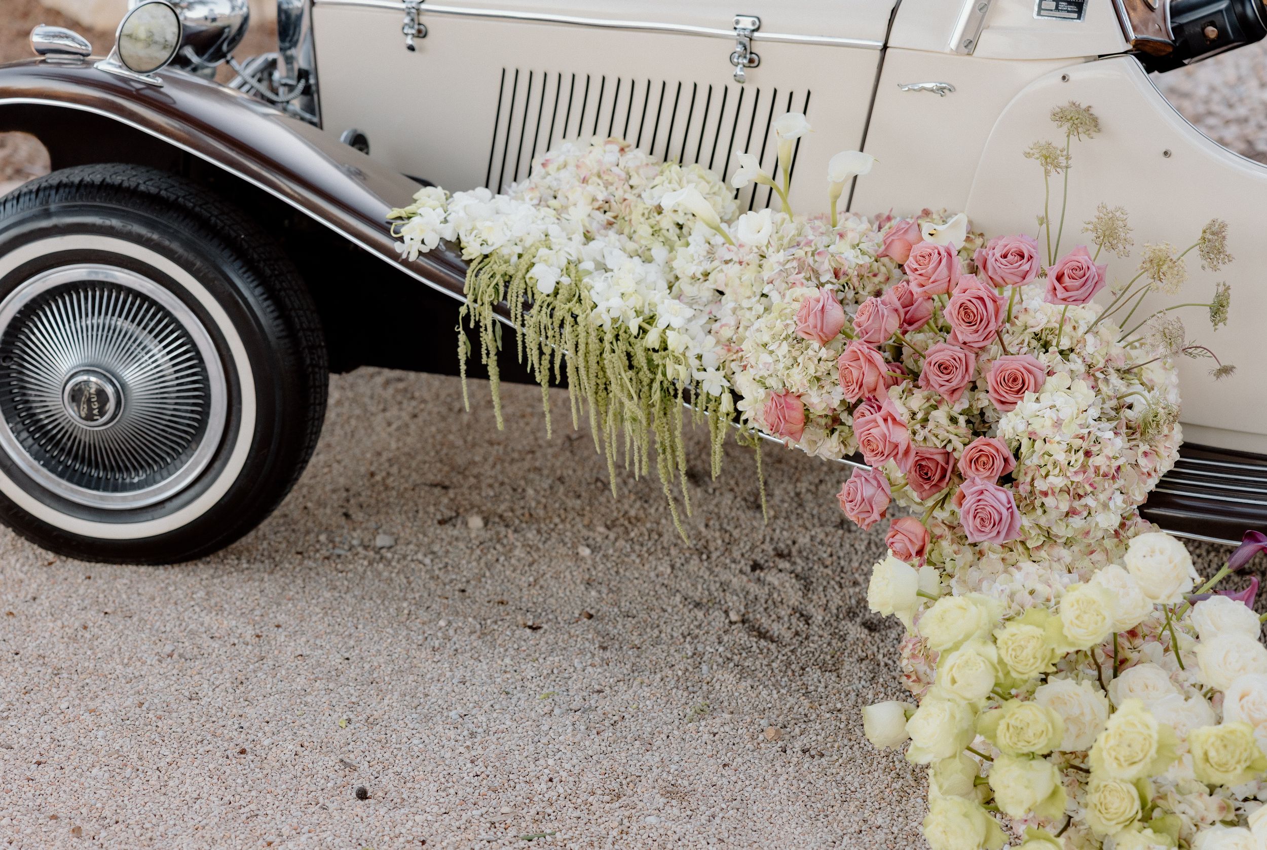 Vintage car adorned with cascading white and pink floral arrangements in an elegant wedding display.