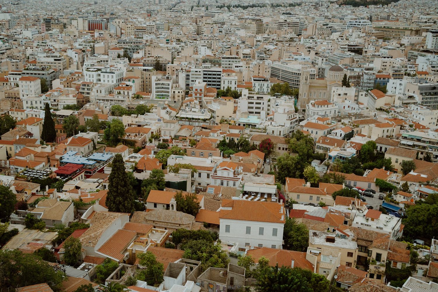 Aerial view of Athens cityscape showing traditional white buildings with terracotta roofs spread across urban landscape.