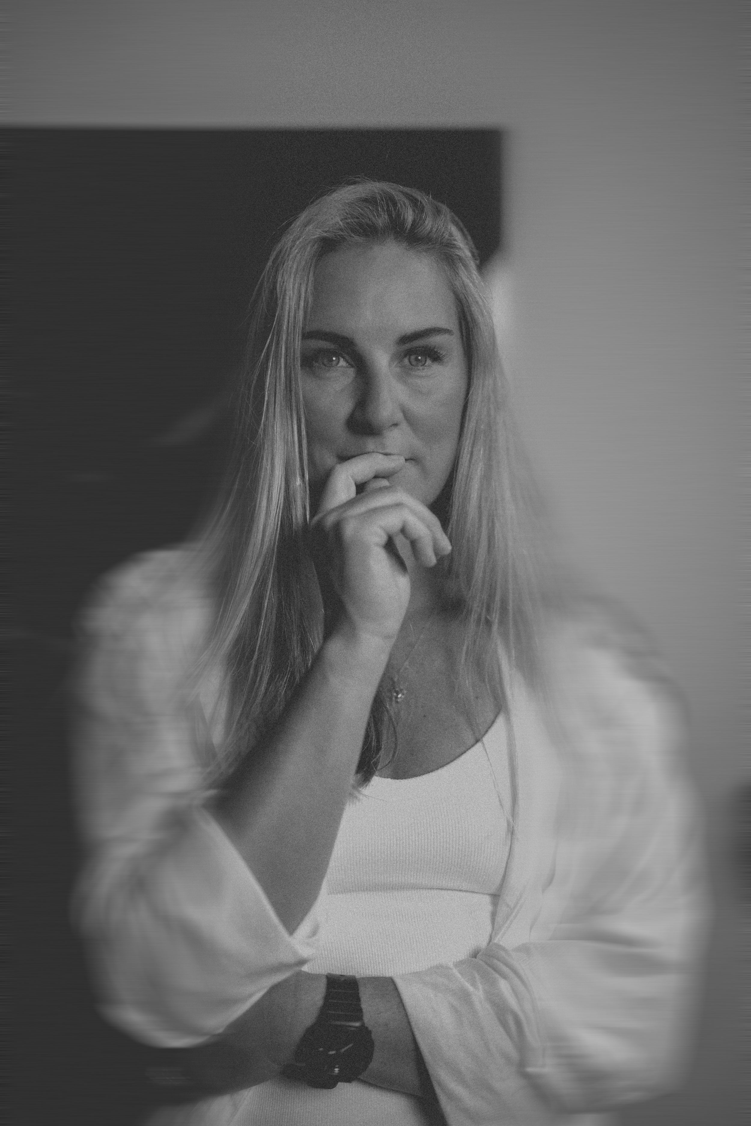 Black and white portrait of a blonde woman in a white outfit, thoughtful pose.