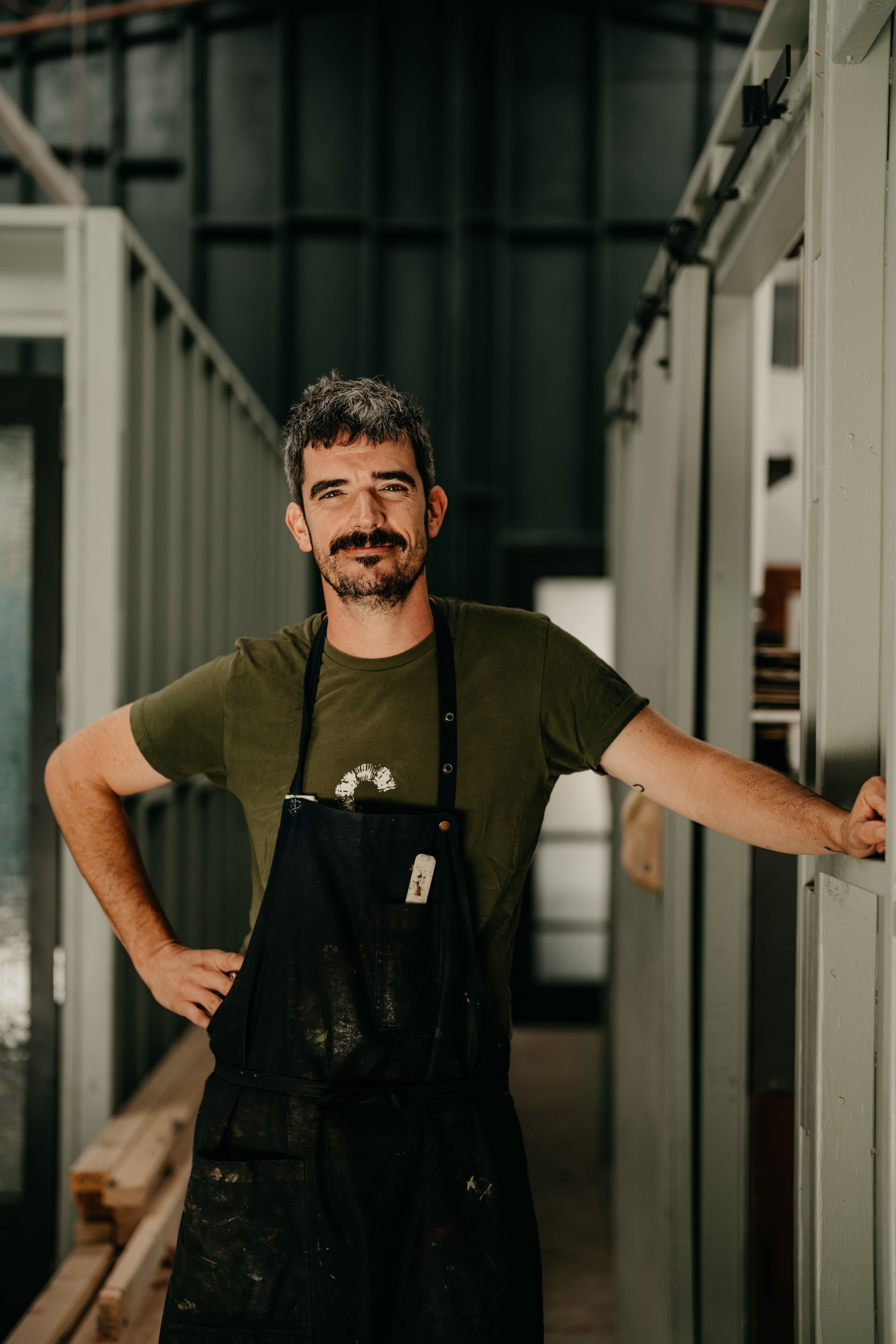 Male craftsman in apron standing in industrial workshop doorway.