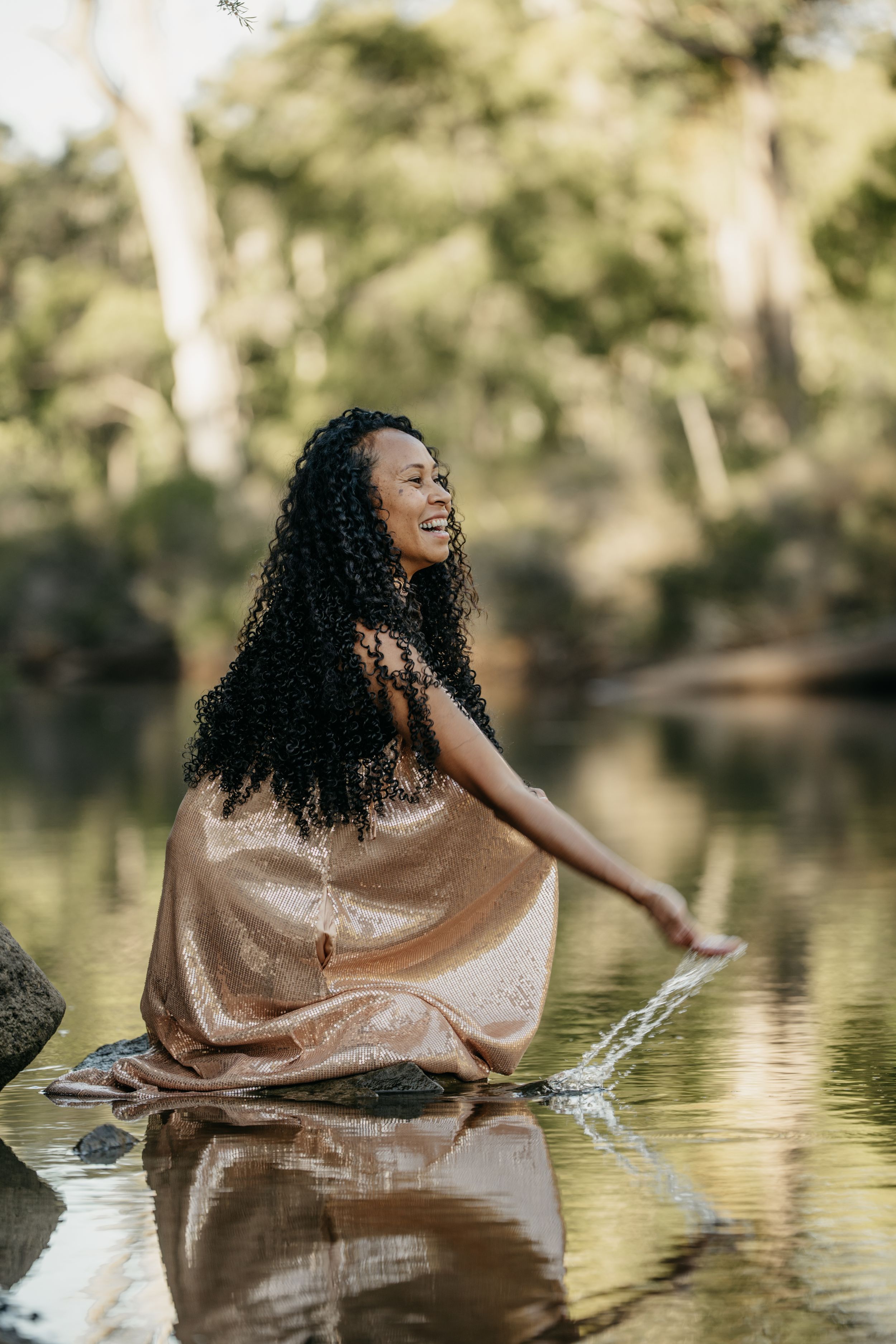 Woman in gold dress playing with water in a serene forest river.
