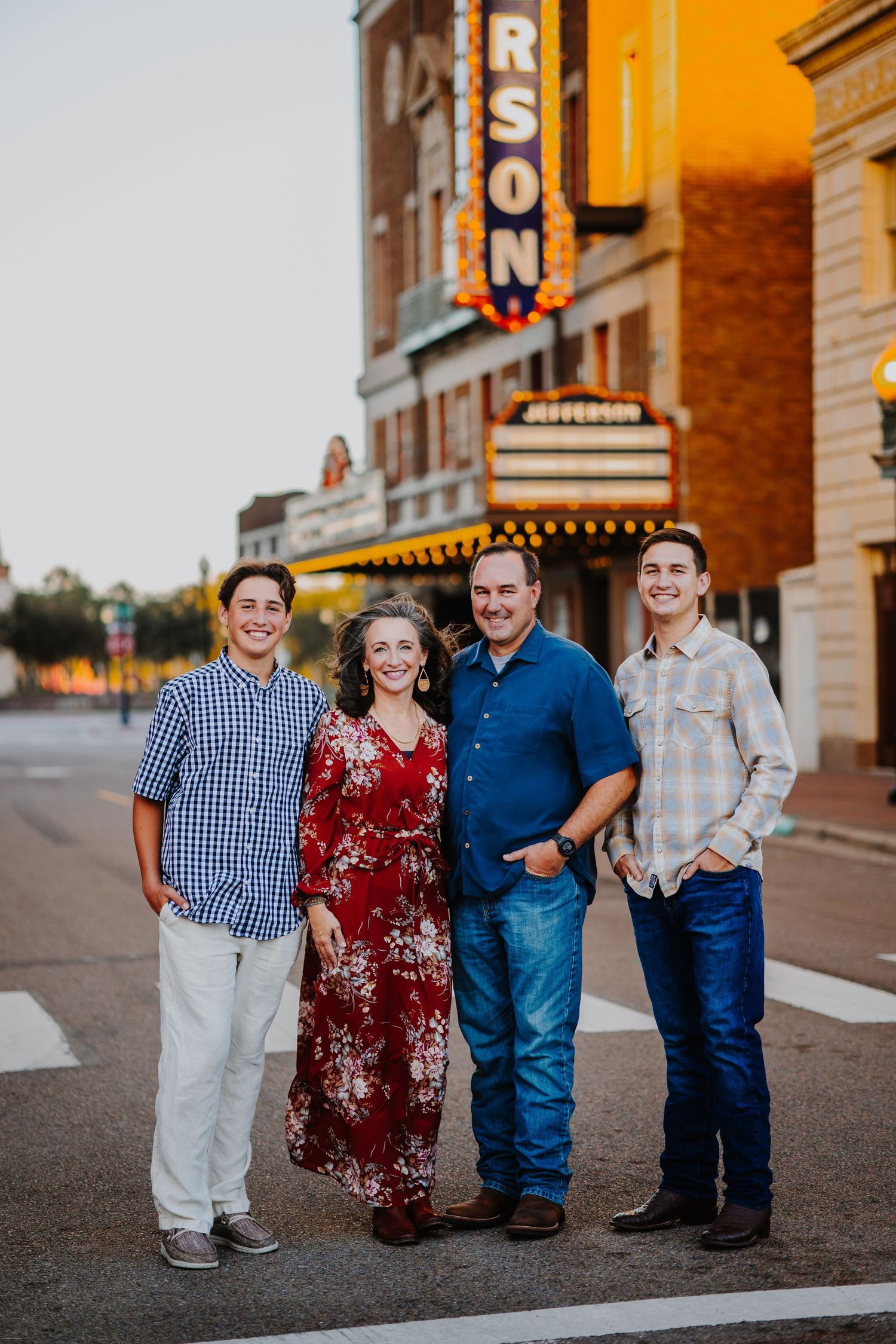 Family group poses for portraits at sunset outside a vintage theater with illuminated signs.