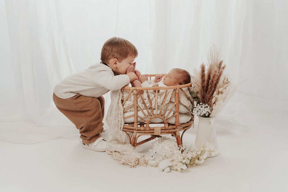 Grand frère et nouveau-né photographiés ensemble lors d'une séance naissance en studio.
