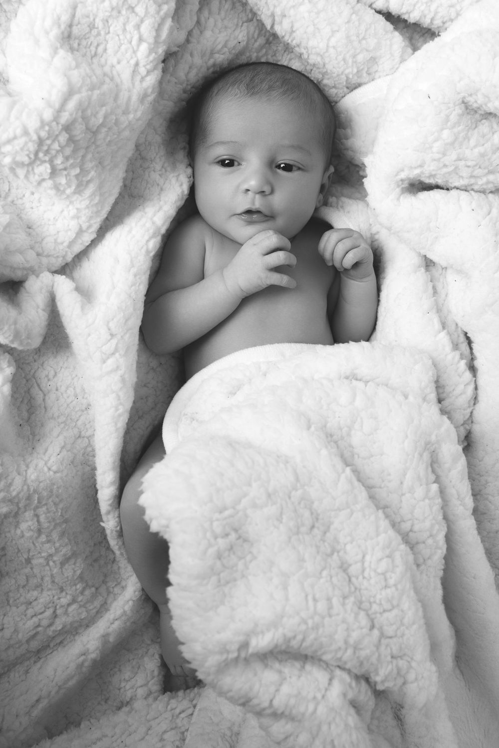 Black and white photo of a peaceful newborn baby wrapped in a soft white fluffy blanket.