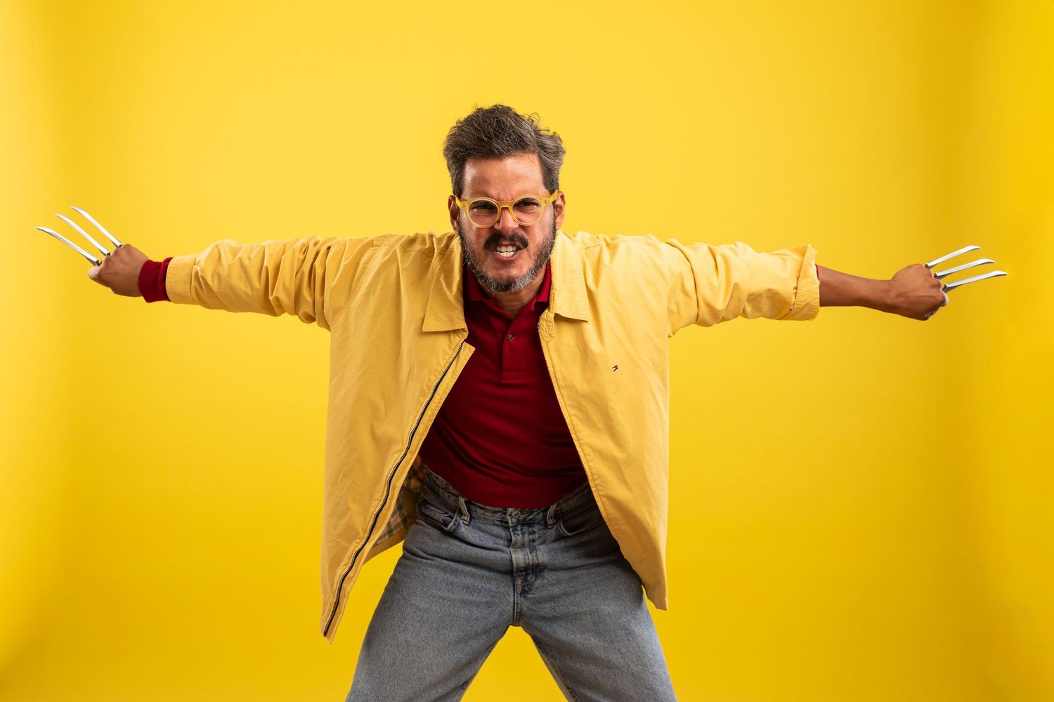 Energetic person in yellow jacket and red shirt poses with outstretched arms against bright yellow background.