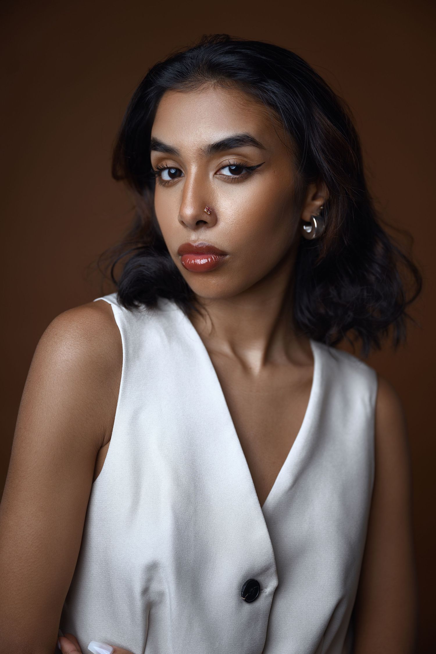 Classic studio portrait featuring bold makeup and white sleeveless garment against brown backdrop.