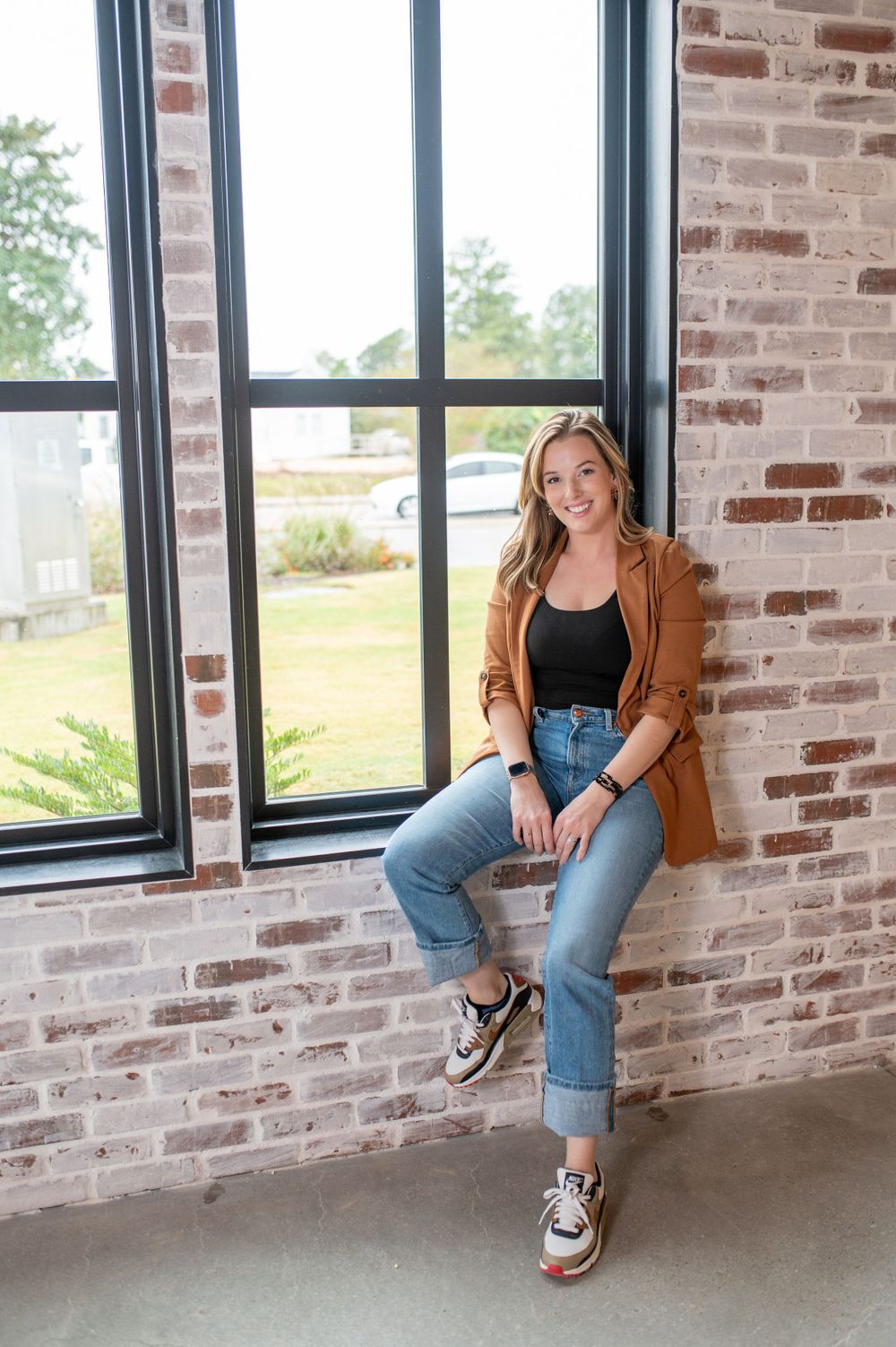 Casual business style with brown blazer and jeans in industrial brick setting.