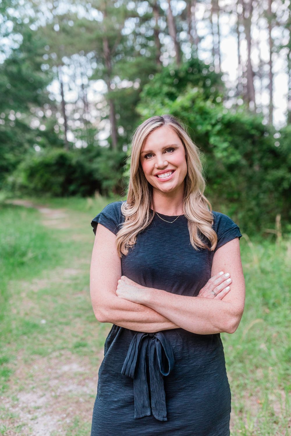 Person in dark dress poses confidently against natural forest backdrop.