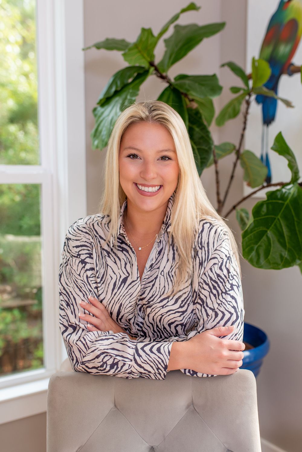 Person in zebra print top posing in modern room with tropical plants and colorful parrot decor at a business branding session.