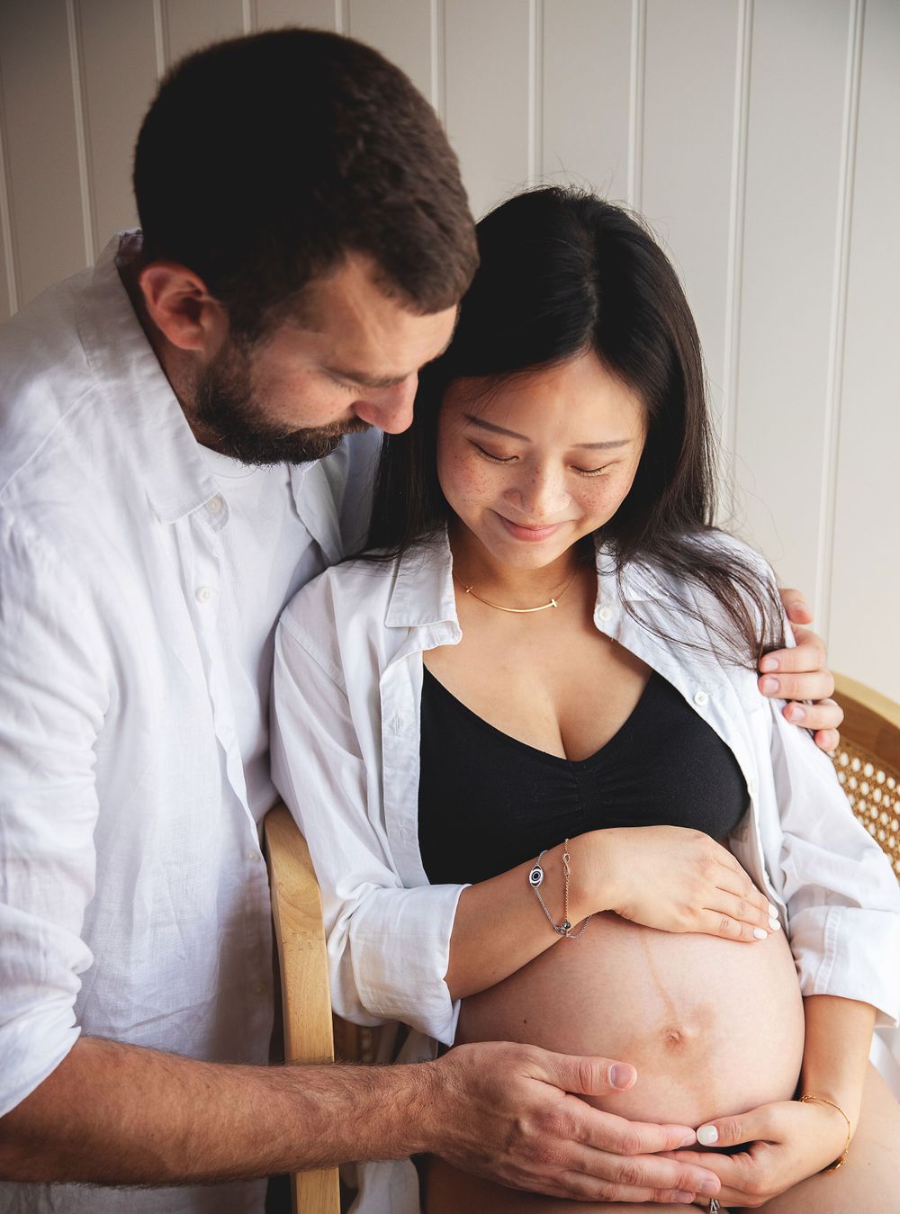 Intimate pregnancy photograph showing a couple in white shirts lovingly embracing and touching a pregnant belly.