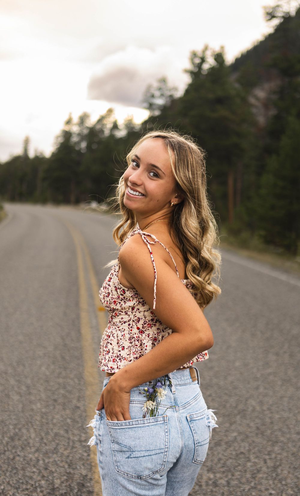 A series of outdoor portraits showing someone in a floral top and denim jeans posing on an empty rural road at sunset.