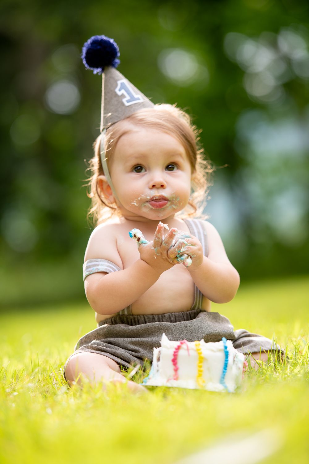 A small child sits on grass during a sunny summer day.