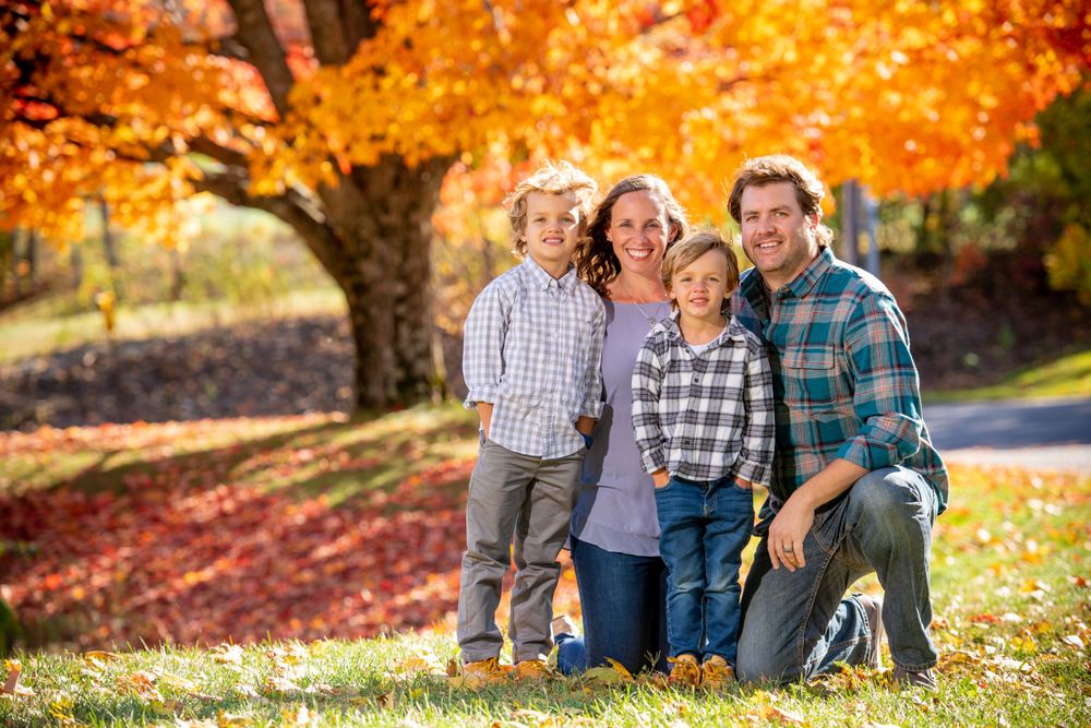 Family group sitting together outdoors with bright orange autumn foliage behind them.