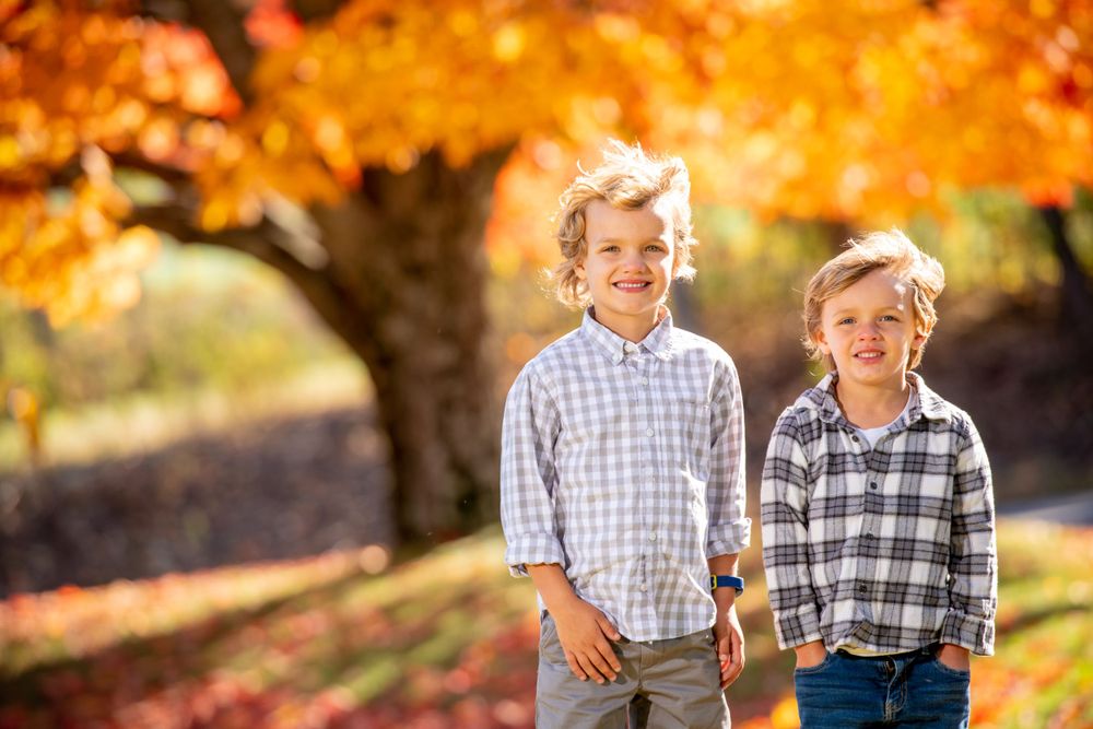 Family members pose together on grass with vibrant fall colors in the background.