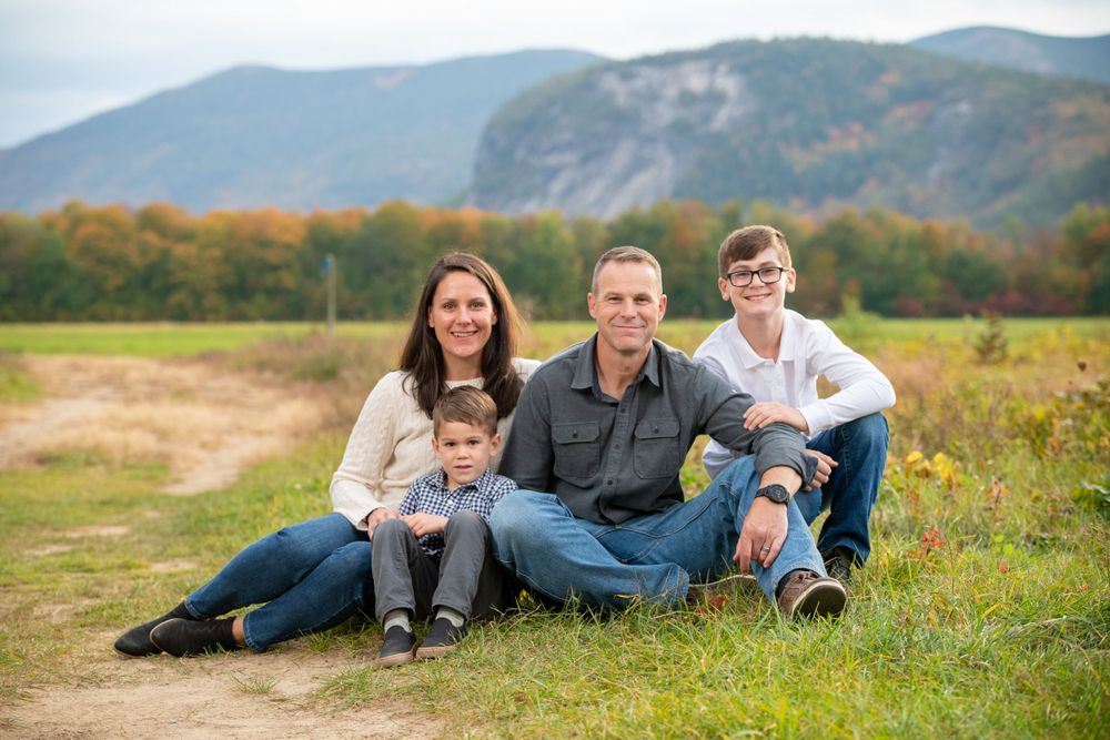 Family lying down together in a grassy field with mountains in the background.