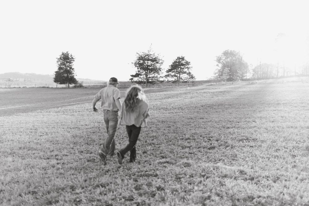 A couple walks hand in hand across a misty field in black and white.