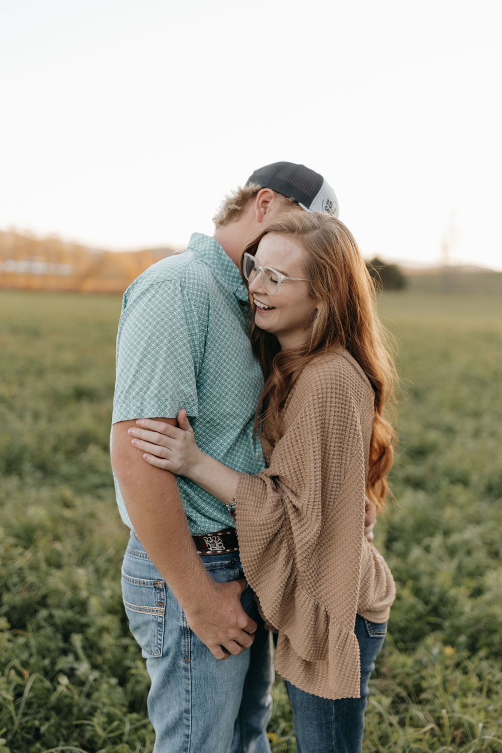 A romantic couple shares an intimate moment while embracing in a sunlit field at golden hour.