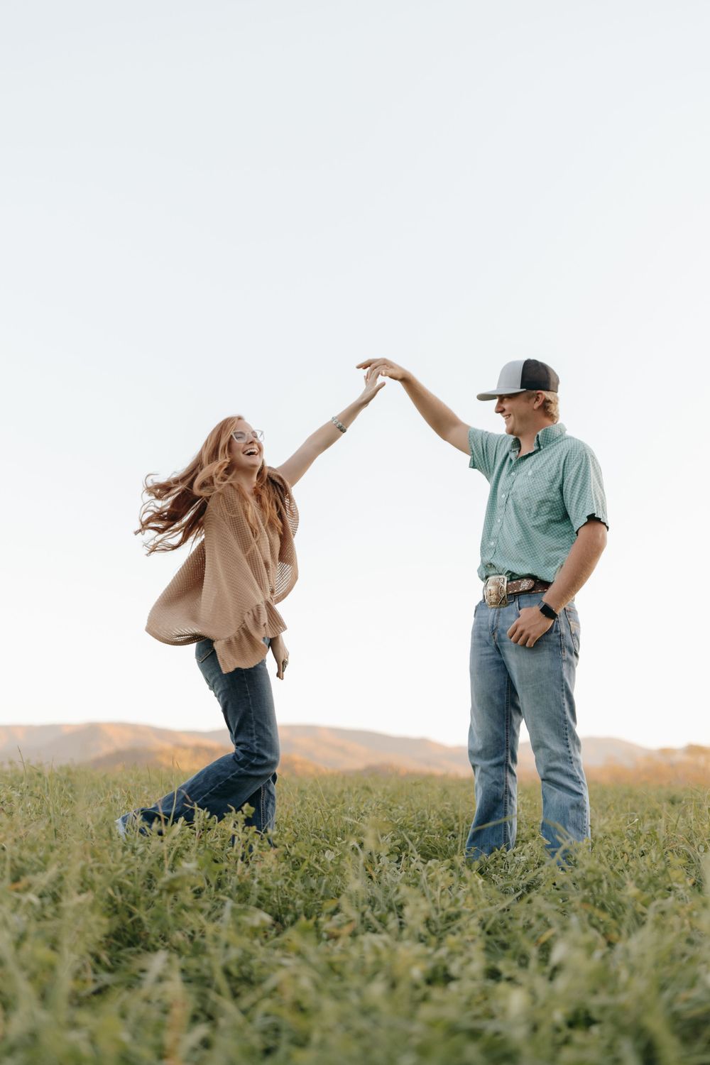A playful couple dances together in a meadow against a bright sky background.