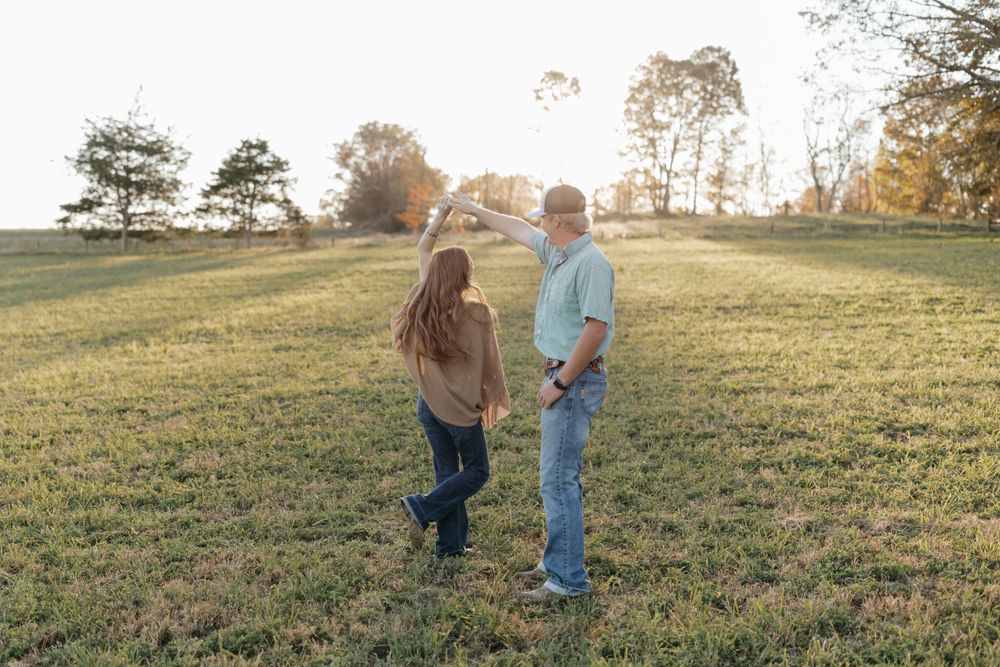 A couple shares a tender moment standing together in a sunlit grassy field.