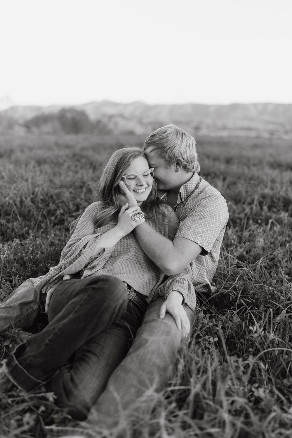 A couple shares a tender moment while lying in tall grass during sunset.