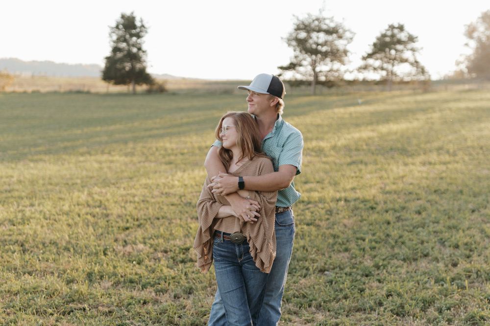 A couple embraces while standing in a scenic hillside field during golden hour.