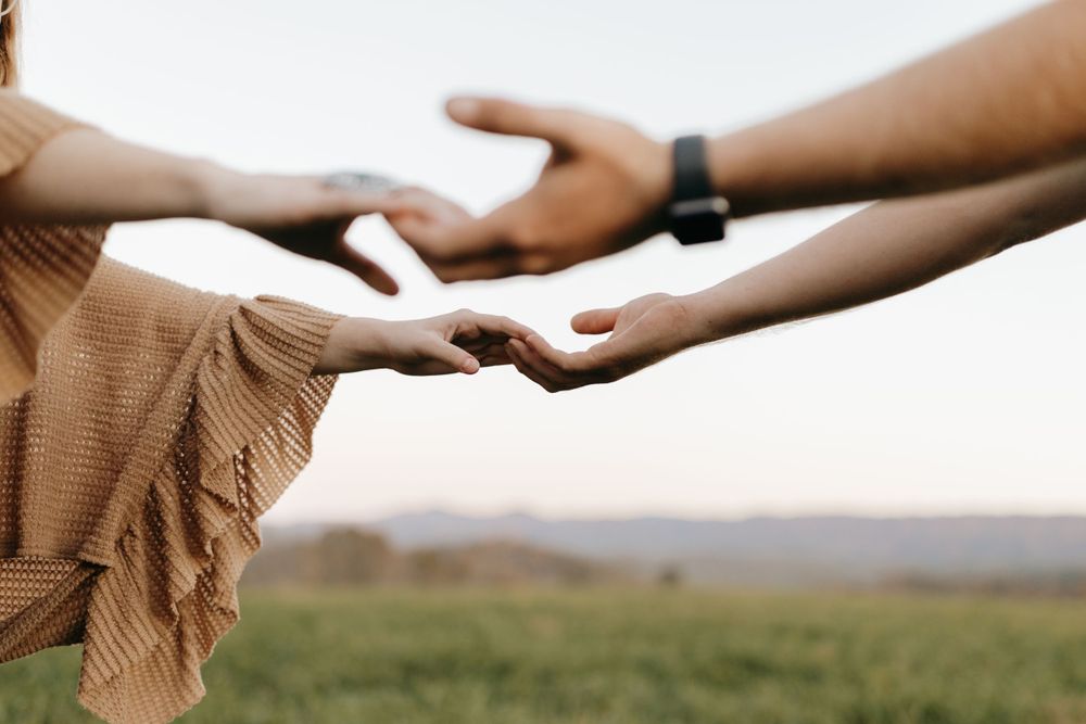 Close-up of two hands reaching toward each other in a field at sunset.