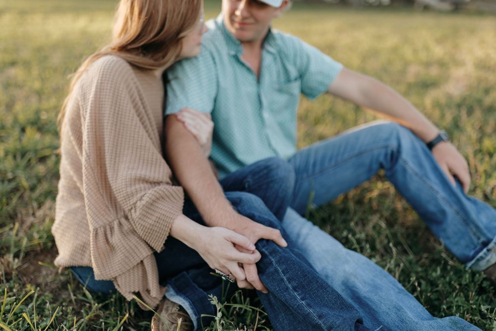 A couple sits casually on grass, engaged in intimate conversation.