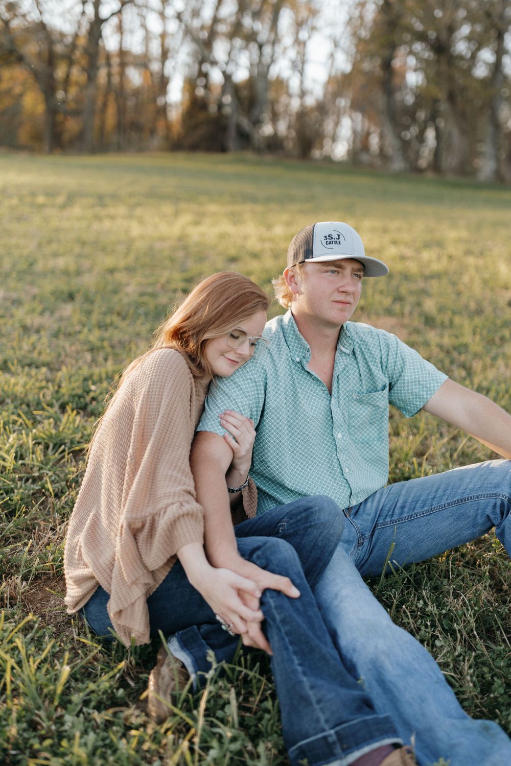 A relaxed couple sits together on grass during golden hour.
