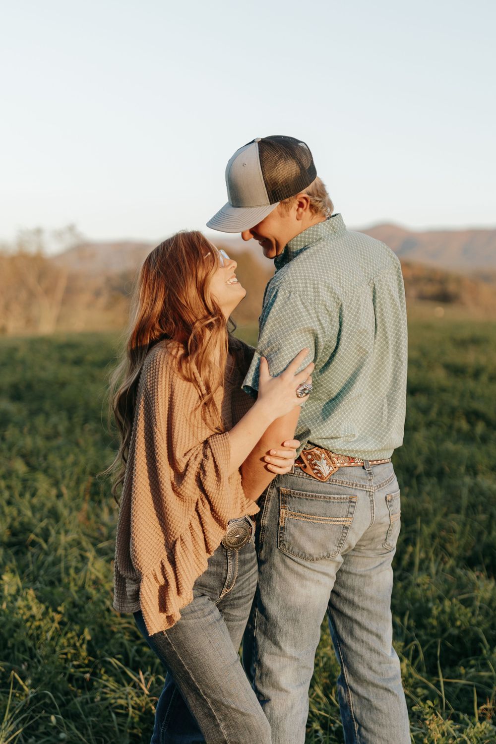 A couple shares an intimate moment while standing in a field at sunset.
