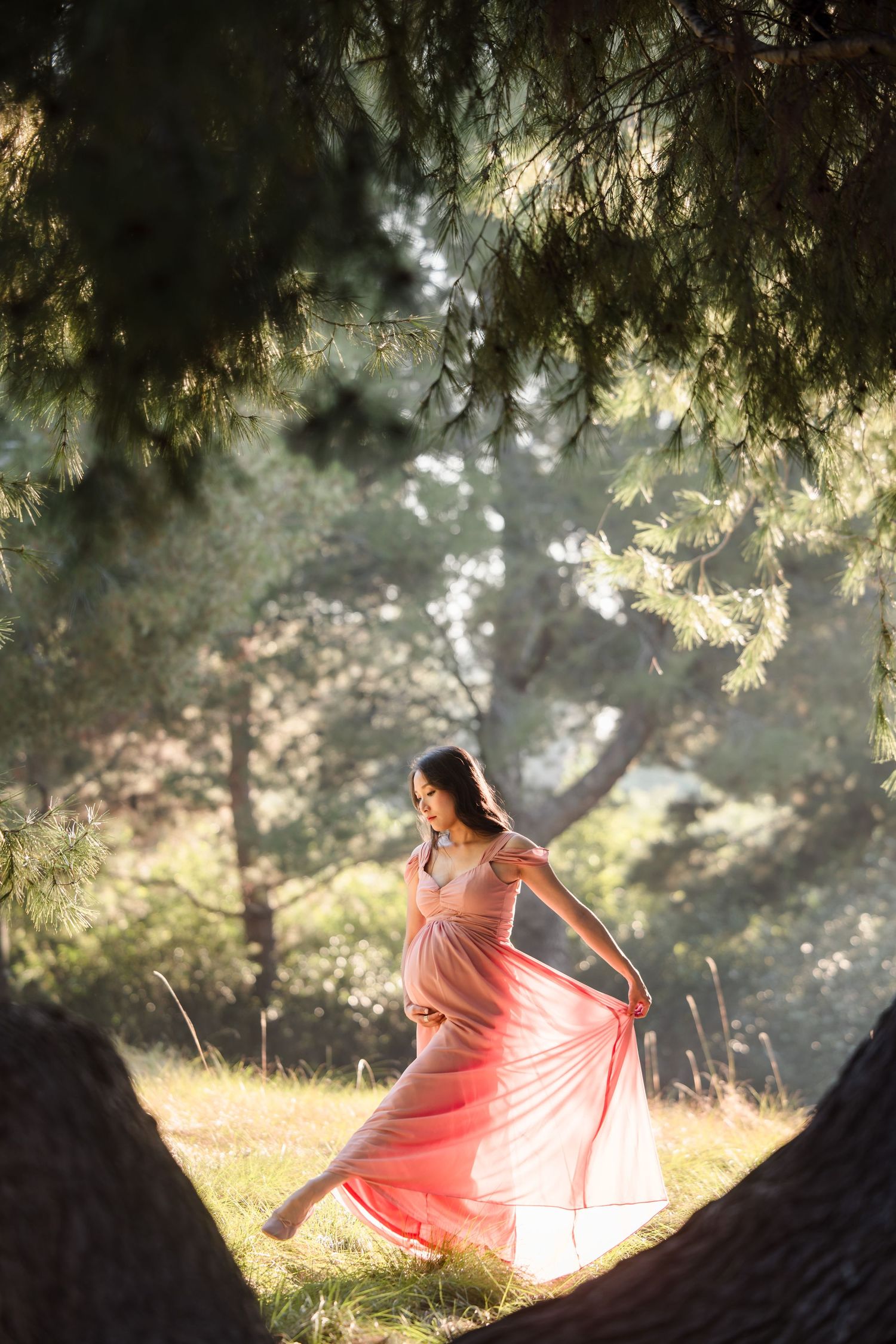 A flowing pink dress twirls gracefully in dappled sunlight filtering through trees in a dreamy outdoor setting.