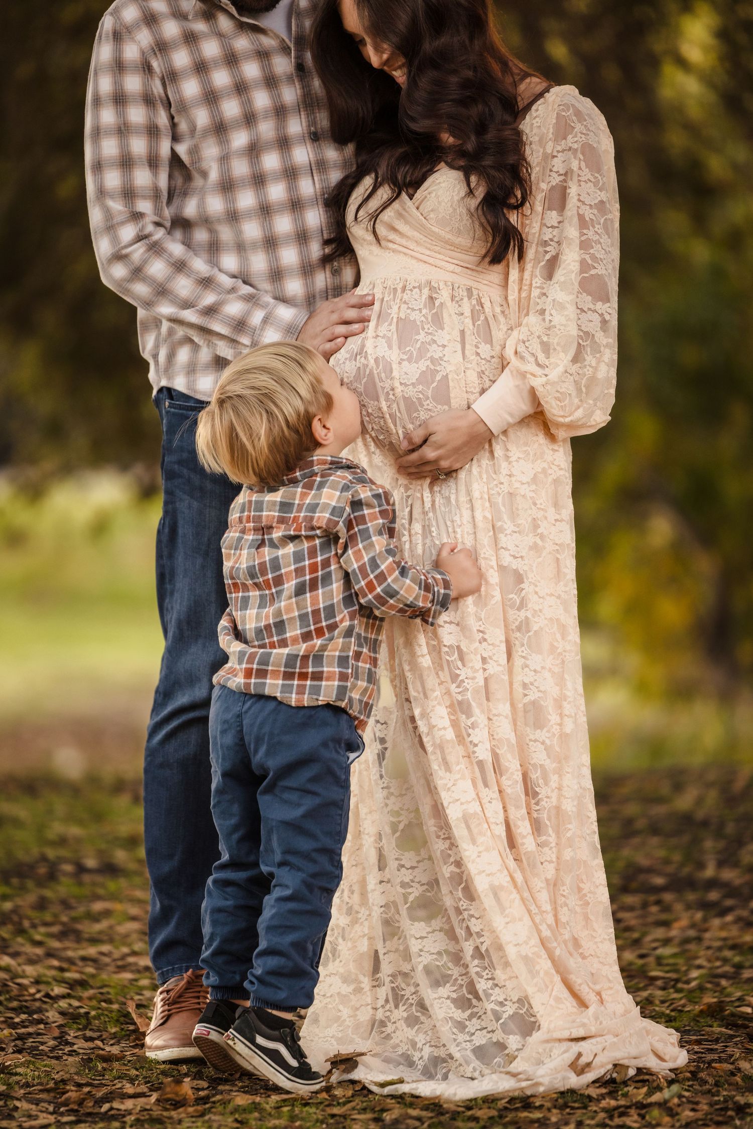 Outdoor family maternity photo with young child touching pregnant mother's belly while wearing matching plaid with father.