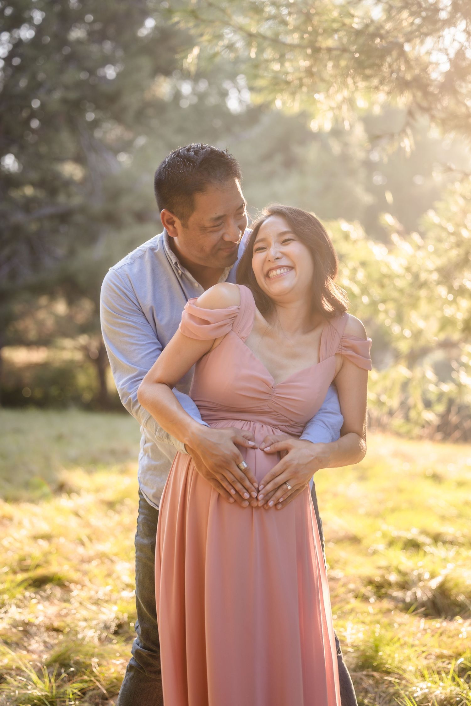 A couple shares an intimate moment at golden hour in a park with sunlit trees in the background.
