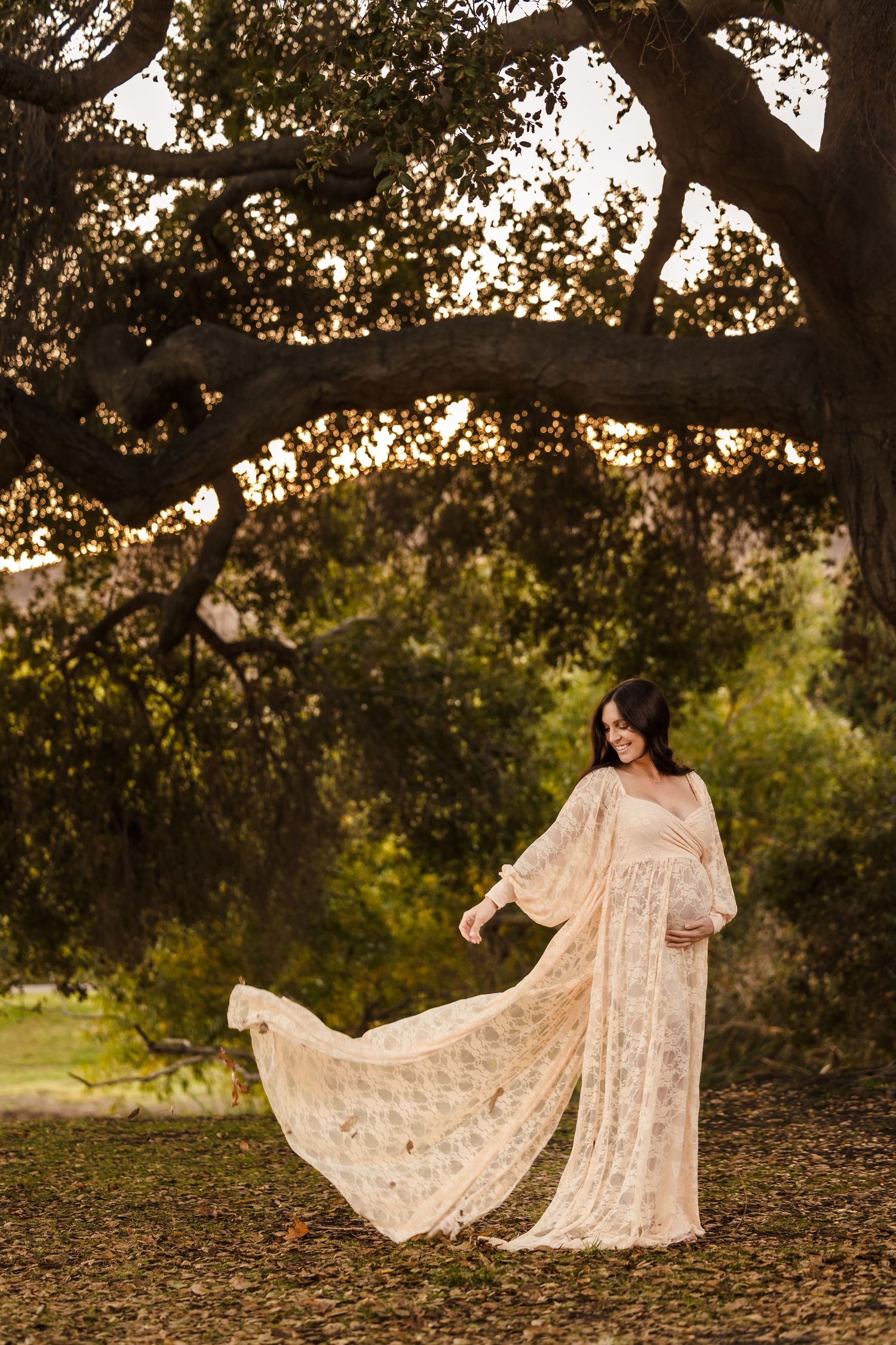 A flowing vintage lace dress catches the golden sunlight beneath a majestic oak tree in a romantic outdoor setting.
