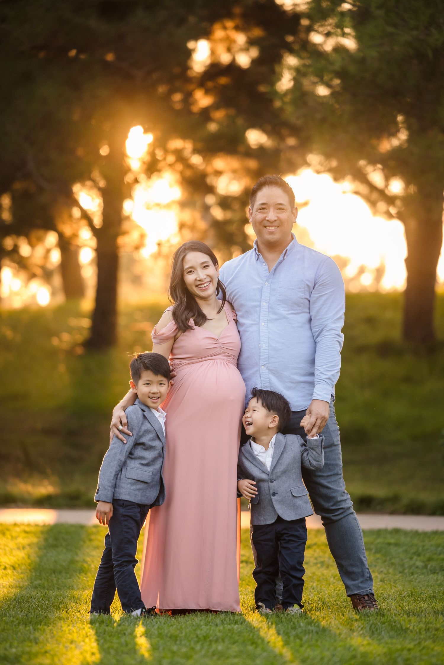 A family of four poses together outdoors during sunset with beautiful golden light filtering through trees.