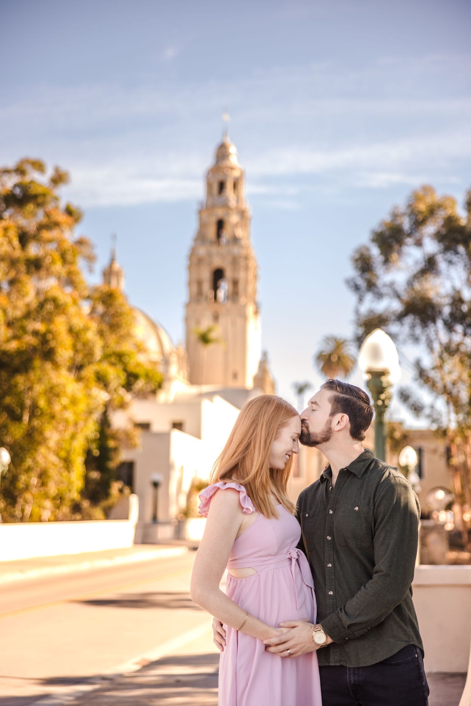 A romantic couple embraces near a Spanish colonial church tower at sunset in Balboa Park, San Diego.