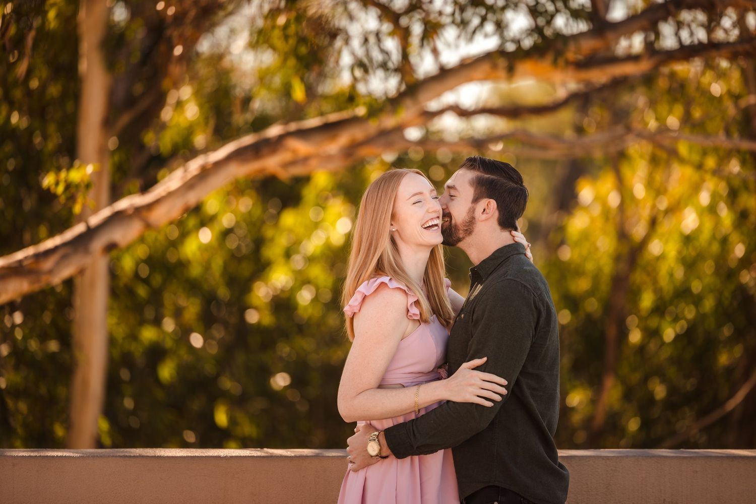 Romantic couple embraces during sunset photoshoot with golden light filtering through trees in background.