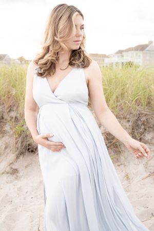 Ethereal beach maternity photos featuring a light blue flowing dress against sandy dunes.