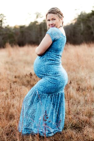 Maternity photos in a field showing a flowing blue lace dress against golden grass at sunset.