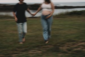 Couple playfully running together on grassy coastal area.