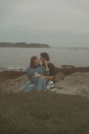 Couple embracing on grassy cliff overlooking misty ocean view.