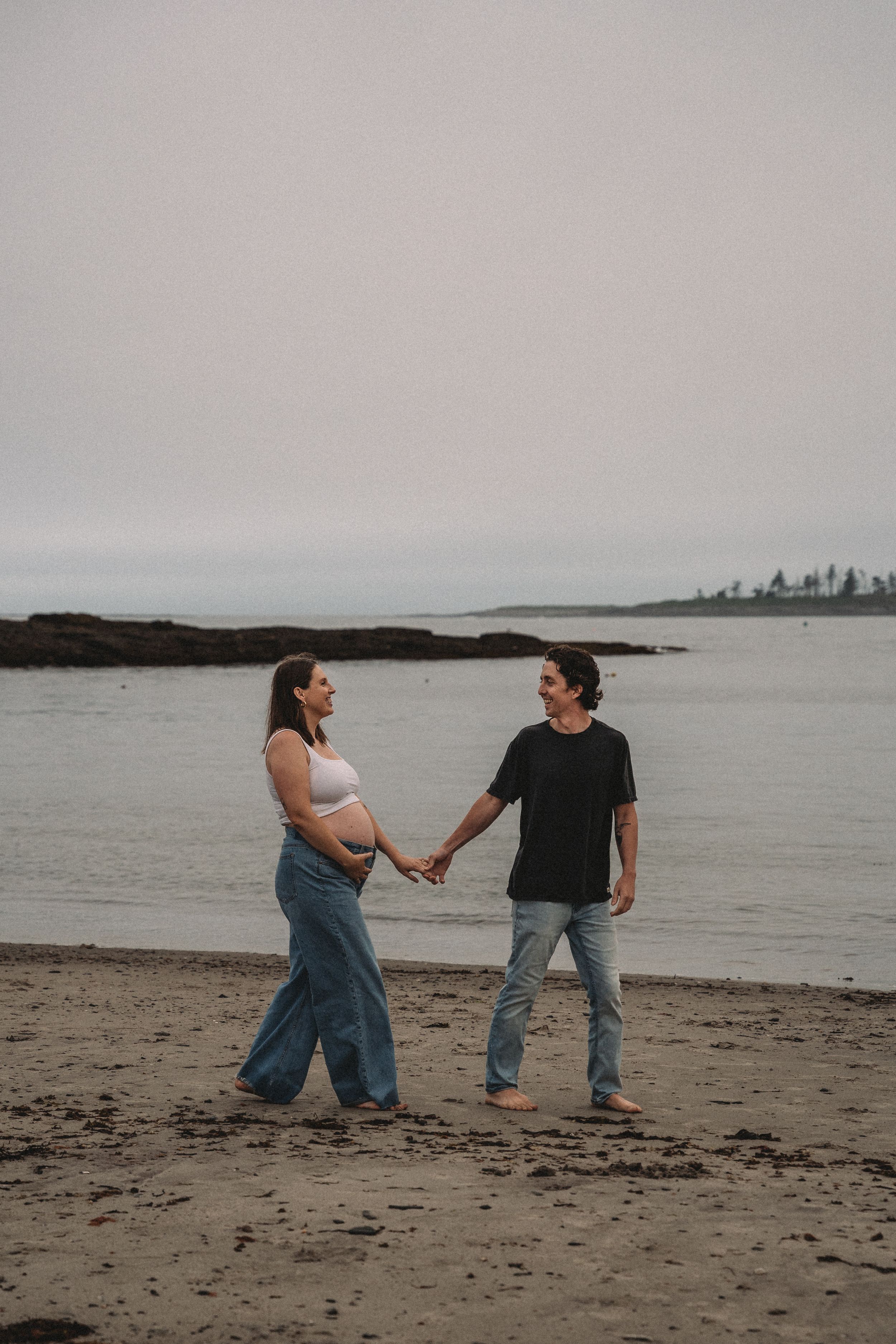 Couple walking and holding hands on a cloudy beach at dusk.