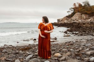 Coastal maternity photos with dramatic rocky shoreline and ocean waves in the background.