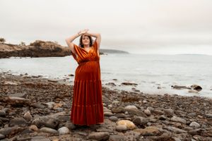 A serene maternity session along a rocky coastline with gentle waves and overcast sky.