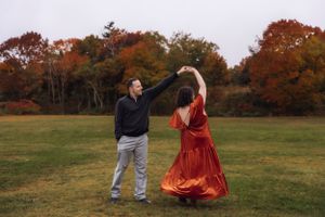 Fall maternity photos in a field with vibrant autumn foliage and a flowing rust-colored dress.