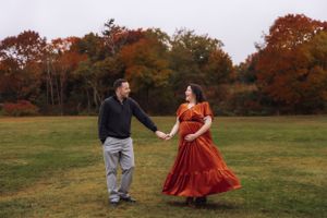 A couple dances in a fall meadow during their maternity photoshoot.