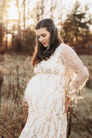 Maternity portraits in golden sunset light featuring woman in white sequined dress.