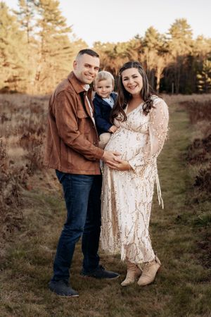 Family maternity session in casual attire against a wooded backdrop at golden hour.