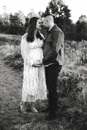A romantic couple embraces in a field wearing white lace and dark clothing in black and white photography.