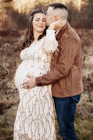 An intimate maternity photoshoot featuring a couple in a rustic outdoor setting.